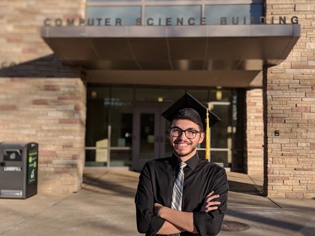 Luis Rodriguez wearing a graduation cap in front of the computer science building.