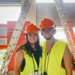 Two people look at the camera in a construction site wearing hard hats