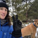 Sam wearing hiking gear in the snow with a dog