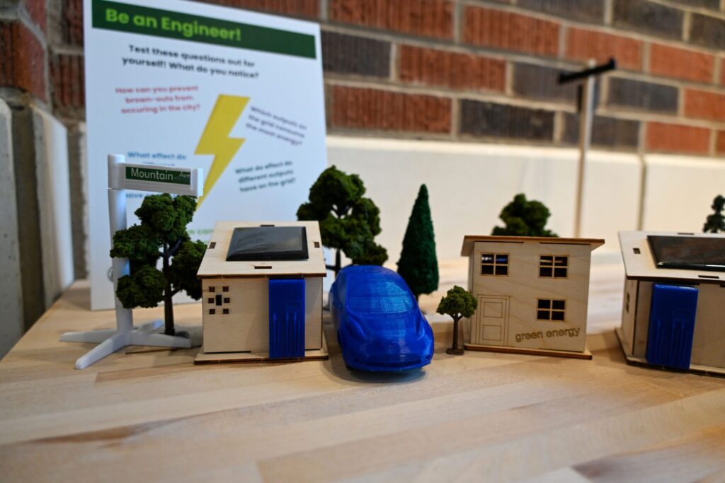 A close up view of parts of the grid kit, including model houses with solar panels and electric vehicles.