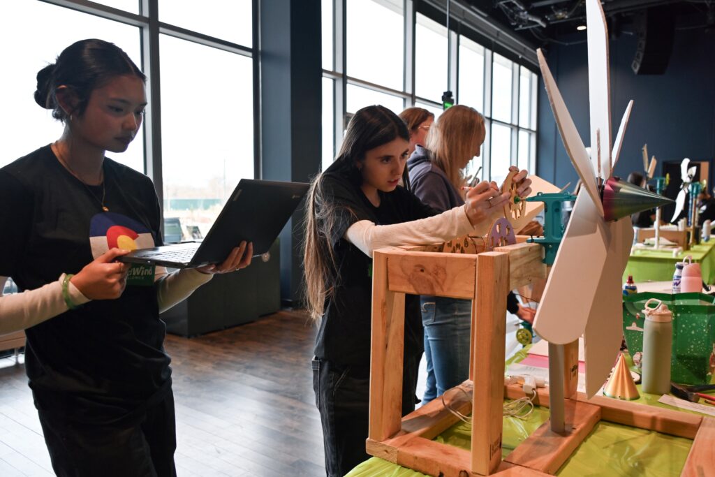 Two participants work on their wind turbine, one is looking at their turbine gears and the other looks at their laptop.