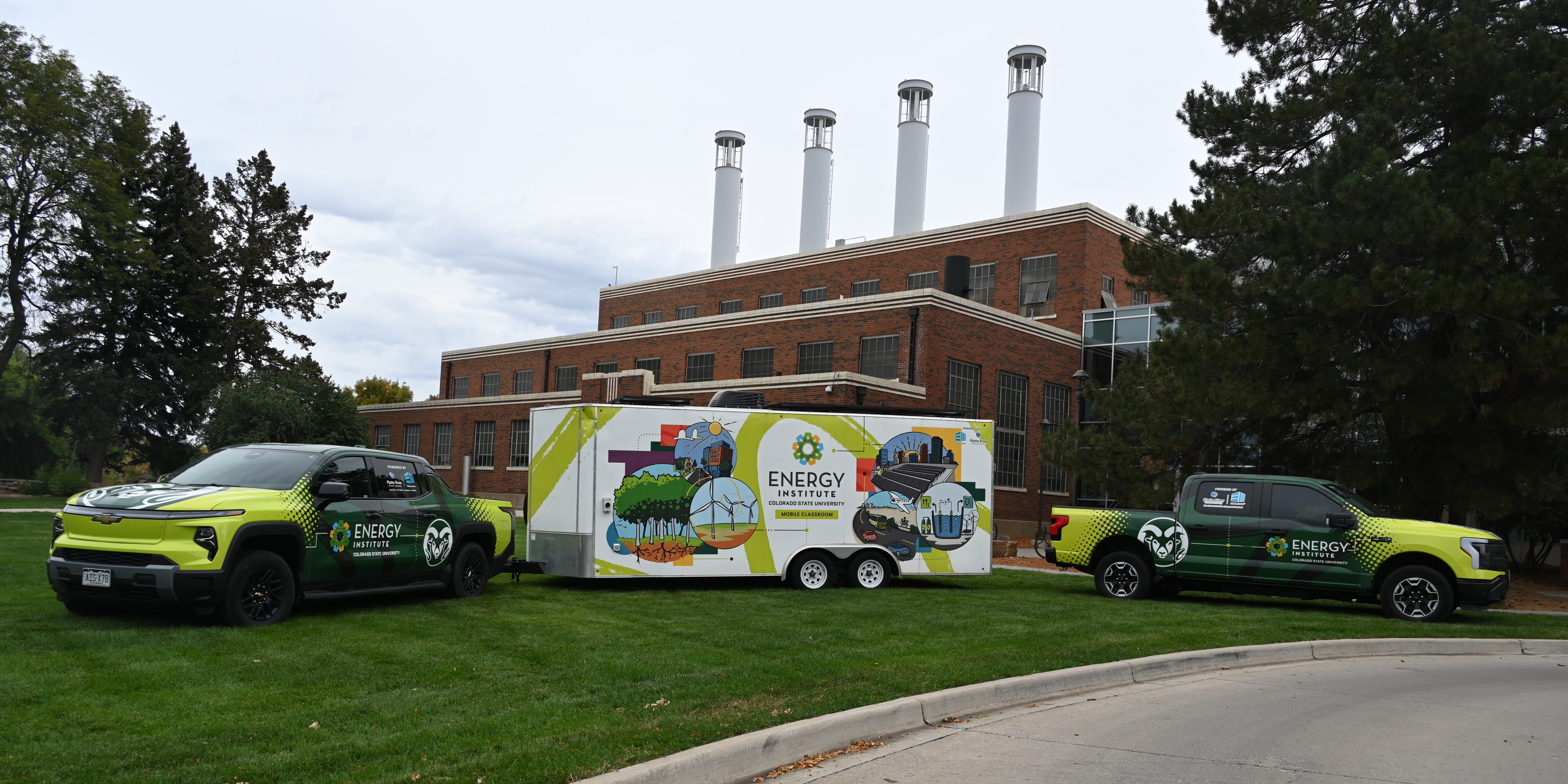 Two Energy Institute branded trucks with the mobile classroom in front of the Powerhouse Energy Campus.