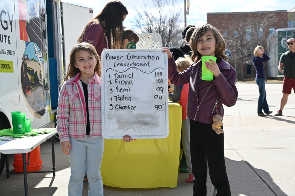 Two children hold a score board at the Mobile Classroom at a community event. 
