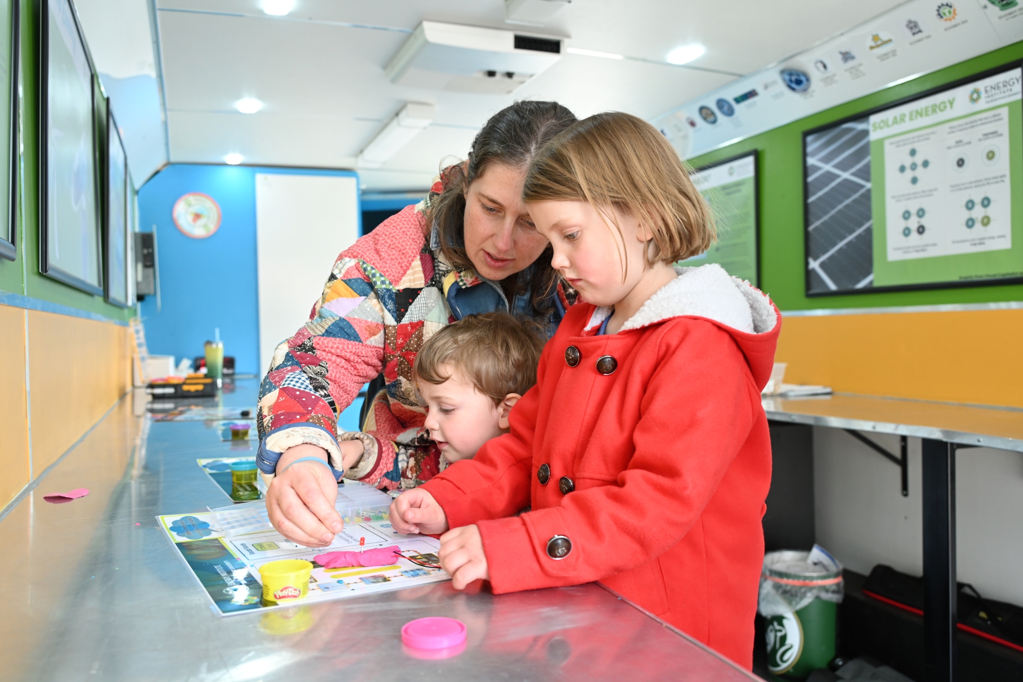 Two children complete an activity with a parent inside the mobile classroom