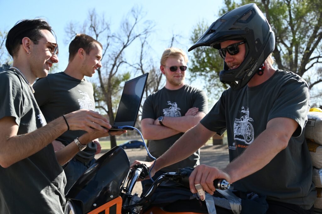4 students. One on a motorcycle. One holding a laptop gathering data from the motorcycle. The other two stand in the background.