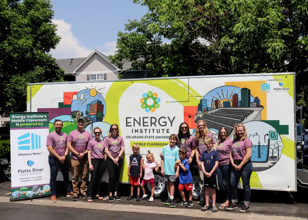A large group stands in front of the mobile classroom