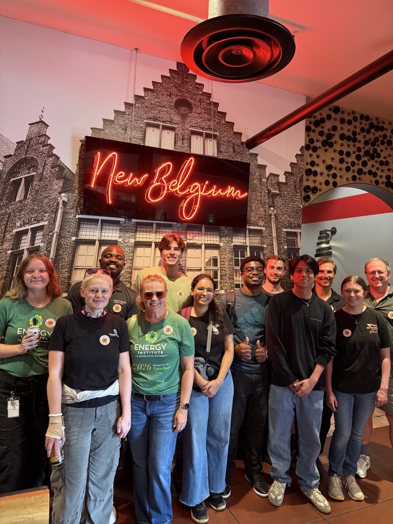 A large group stands in front of a neon "New Belgium" sign