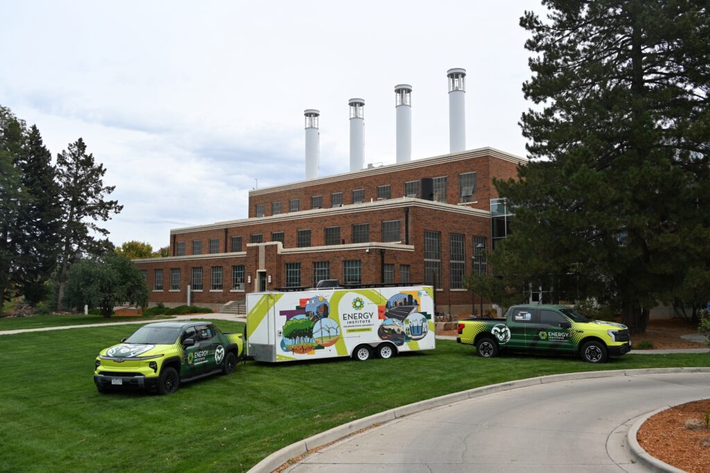 The mobile classroom trailer and two Energy Institute branded electric trucks in front of the Powerhouse.