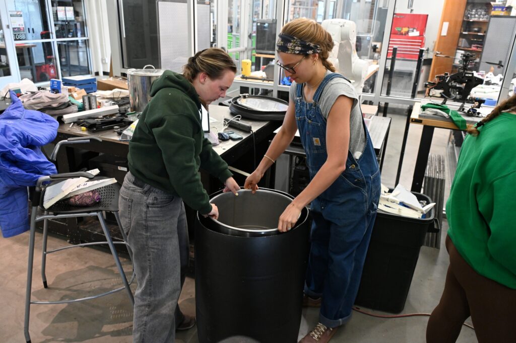 Two students put a drum into a large container